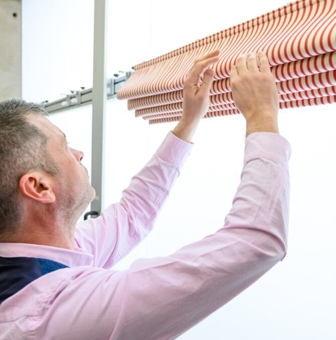 Inspecting red striped Roman blind in a workshop