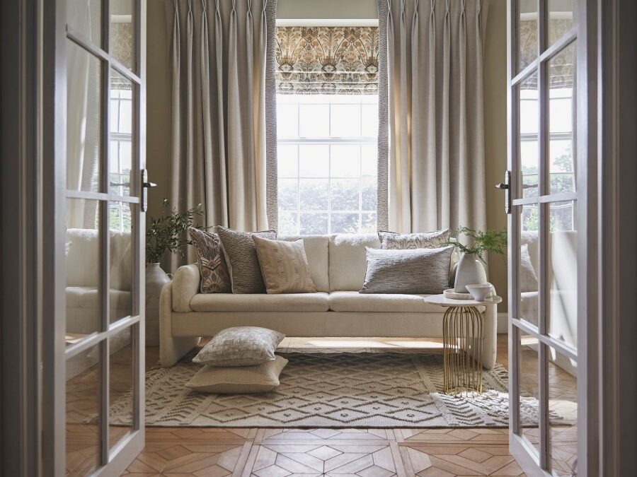 Elegant living room with beige curtains, patterned Roman blind, neutral sofa, and decorative cushions.
