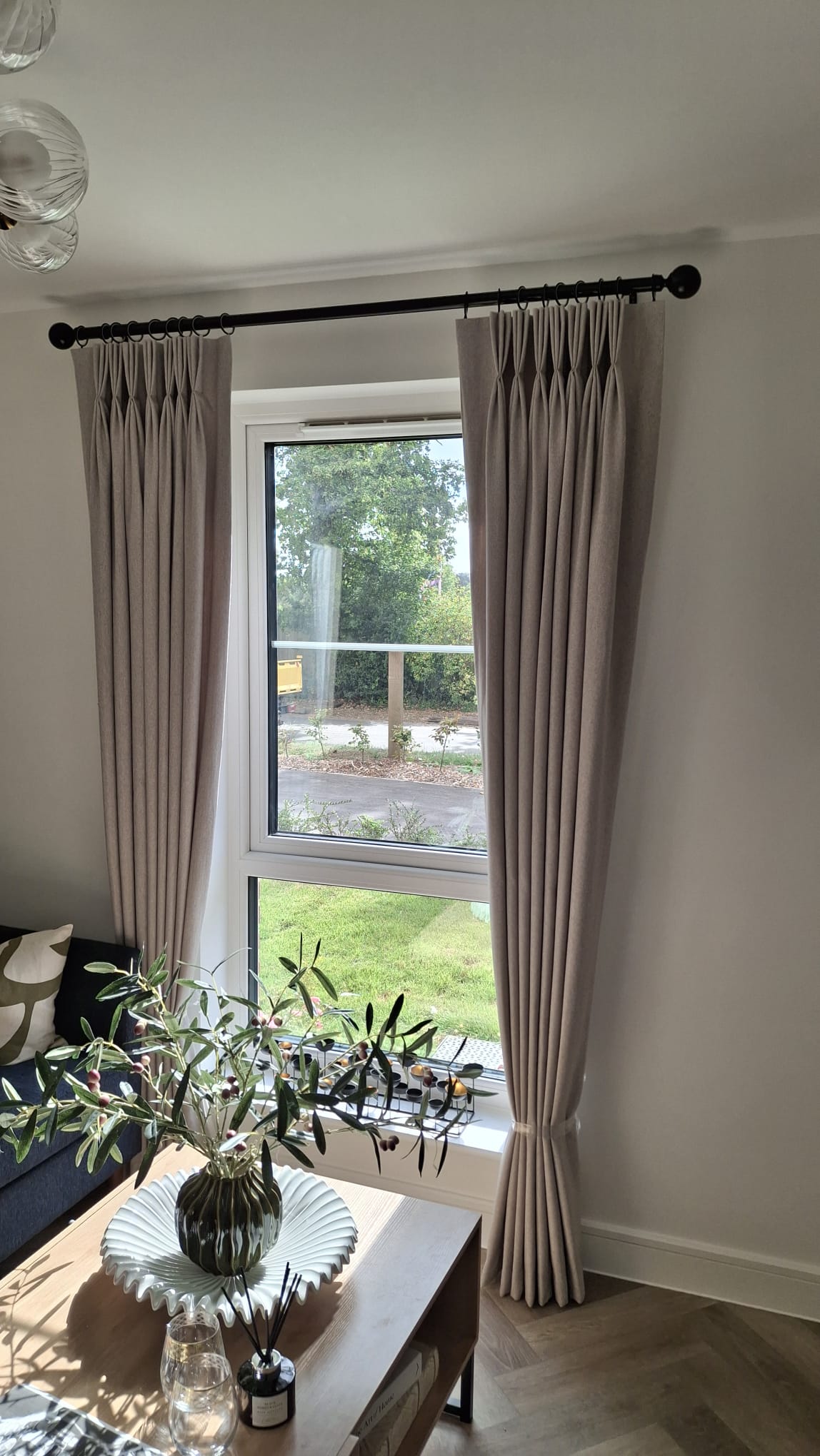 Neutral beige pinch pleat curtains on black curtain pole in modern living room Neutral beige pinch pleat curtains on black curtain pole in modern living room